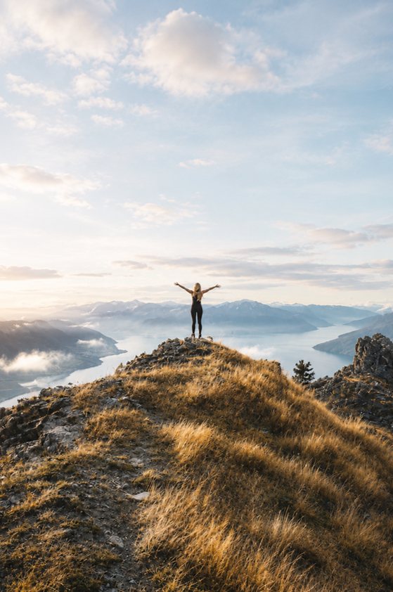A person atop a misty mountain at sunrise with arms raised